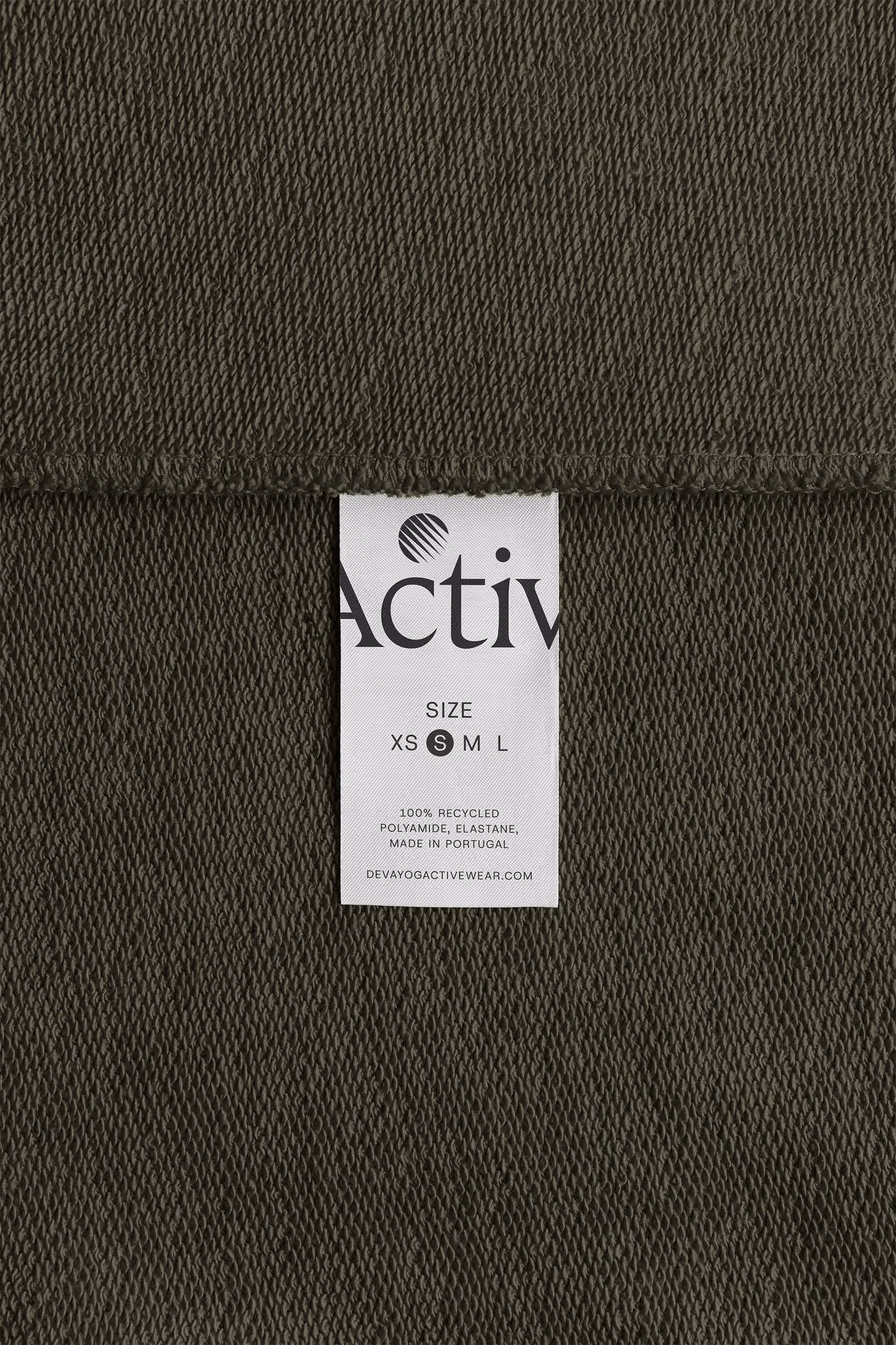 White woven label with the new Deva symbol, a cropped ‘Activ’ wordmark, size S marked and ‘Made in Portugal’, sewn onto olive fleece.